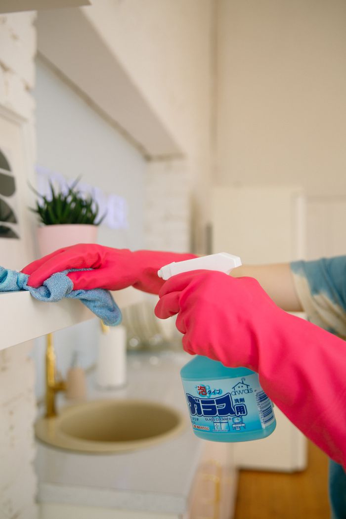 journey-02 Person using spray bottle and cloth for cleaning a kitchen shelf, ensuring hygiene and cleanliness.